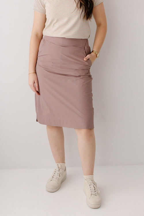 Person wearing a mauve skirt and white sneakers on a plain background